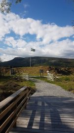 Svenska flaggan är hissad inne i Långå Skans. I förgrunden syns bron över Vallgravsbäcken och jordvallarna runt skansen. Foto: Liselott Prestjan
